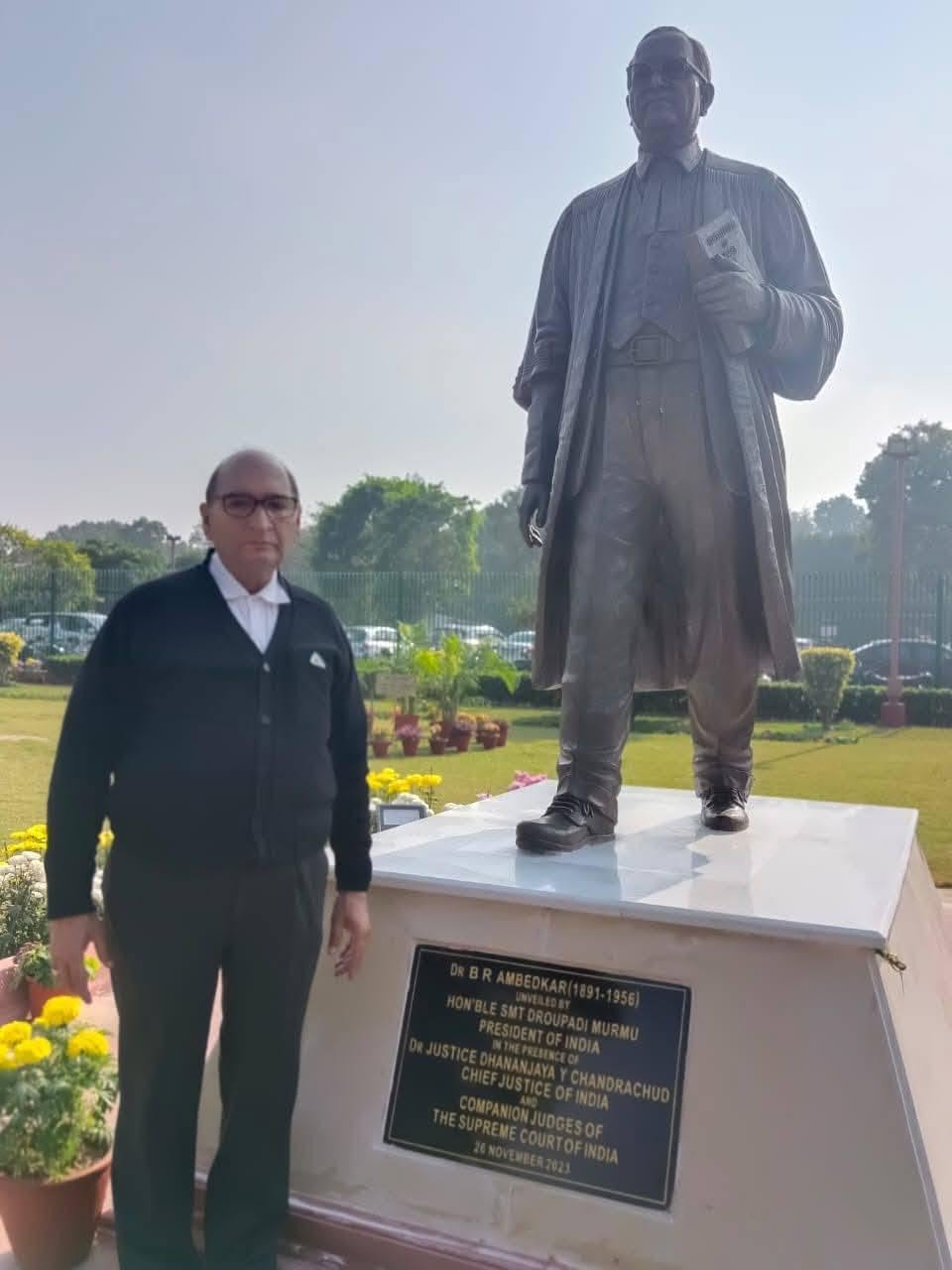 Advocate Vijay Sharma in formal advocate attire beside a commemorative statue